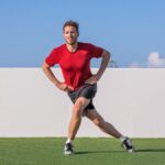 Man outdoors on grass performing a single leg squat variation with hands on hips and right leg extended behind left