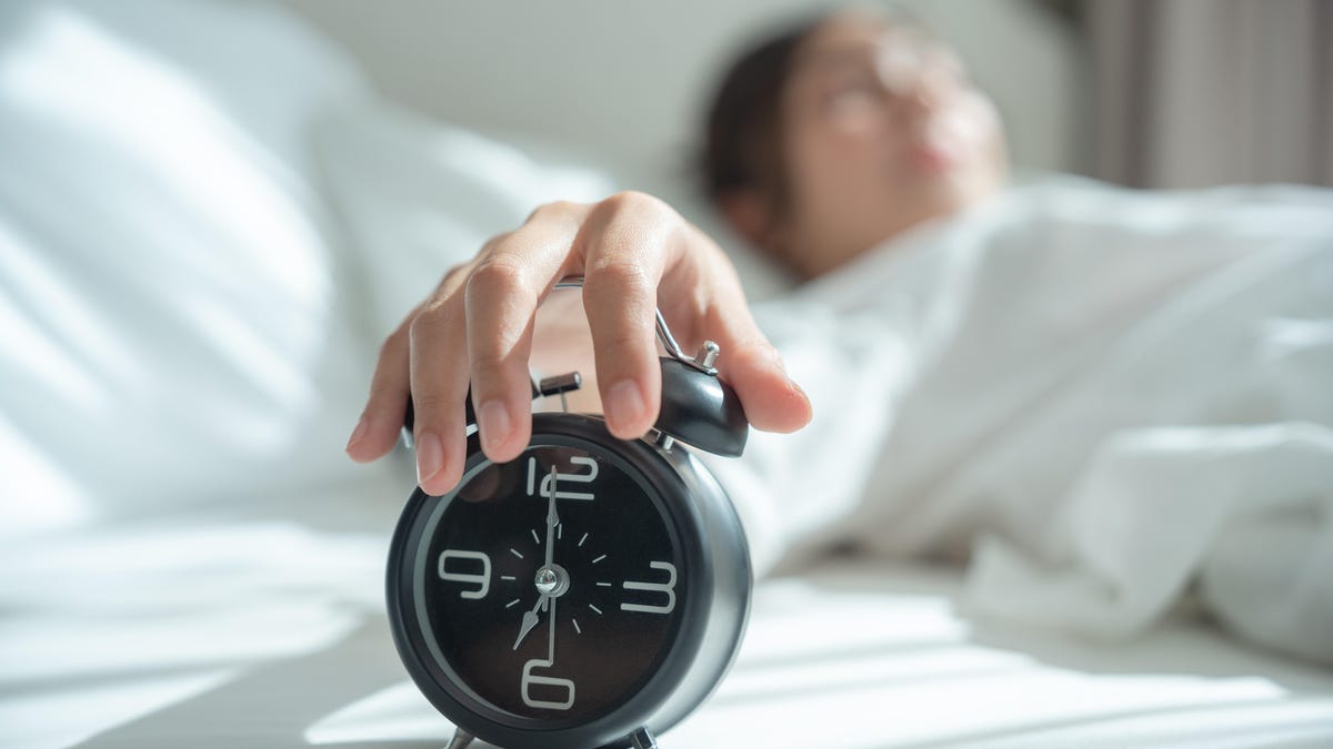 A woman hitting snooze on an alarm