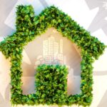A frame of a house created with green leaves is overlaid on symbols of recycling, solar panels, repairs and electricity