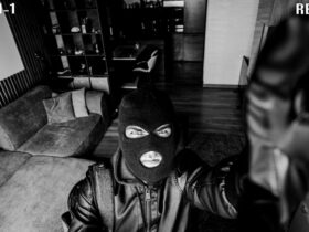 Mock picture of a security cam capturing a black-and-white image of a masked burglar fiddling with the lens.