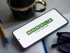 Wordle game shown in a phone with sunglasses, coffee cup, pen